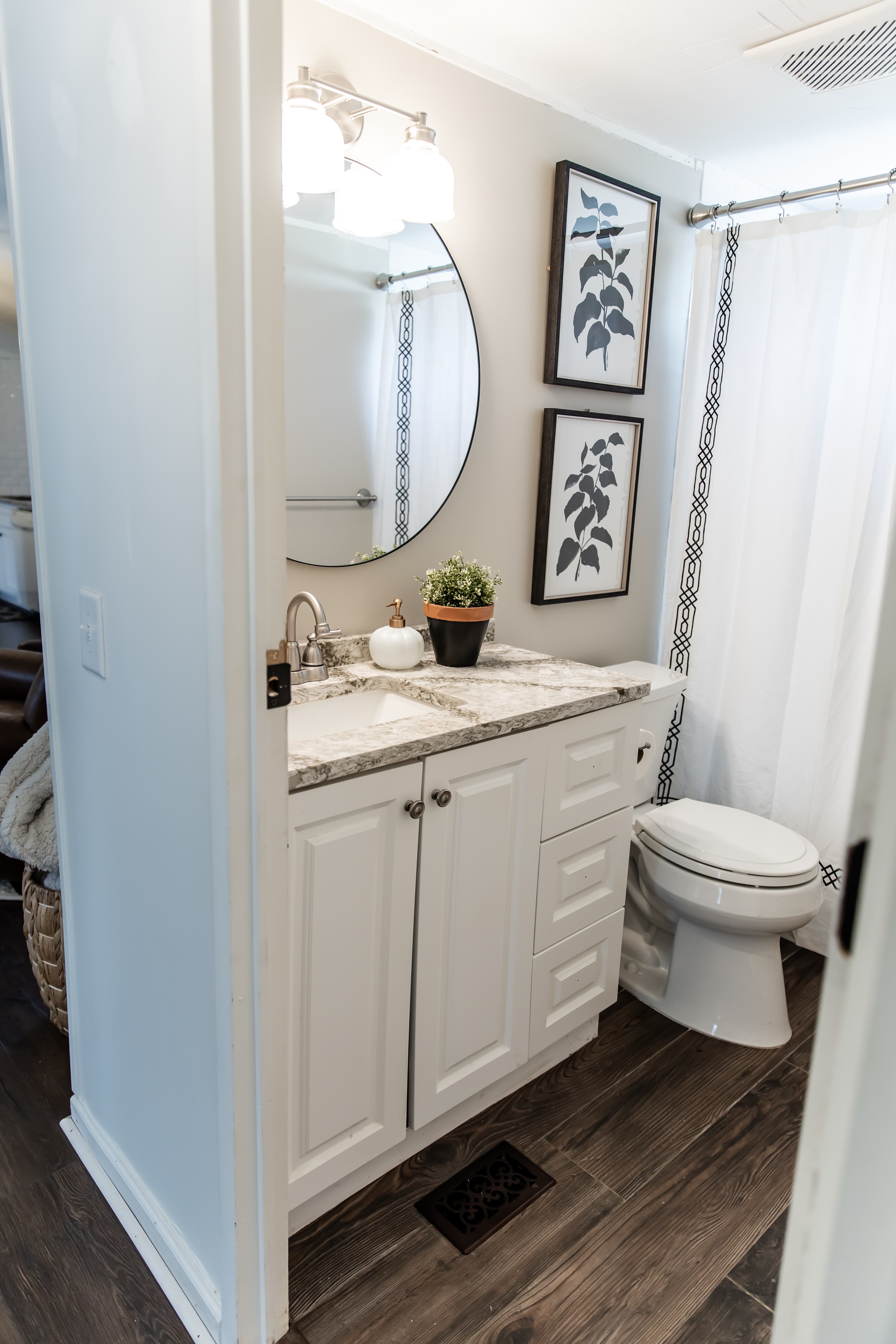 A modern bathroom featuring a white vanity, round mirror, wall art, and a shower curtain.