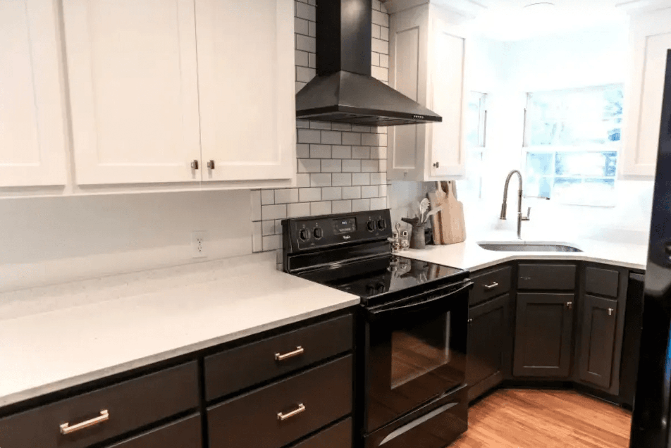 Modern kitchen with white and black cabinetry, stainless steel appliances, and a corner sink.