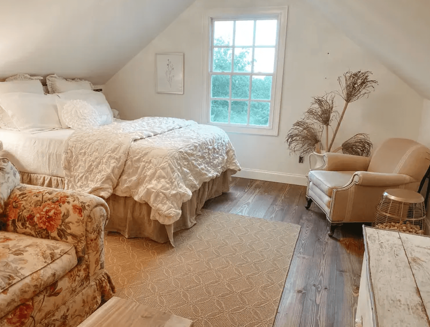 Cozy attic bedroom with a large bed, floral couch, and a window letting in natural light.