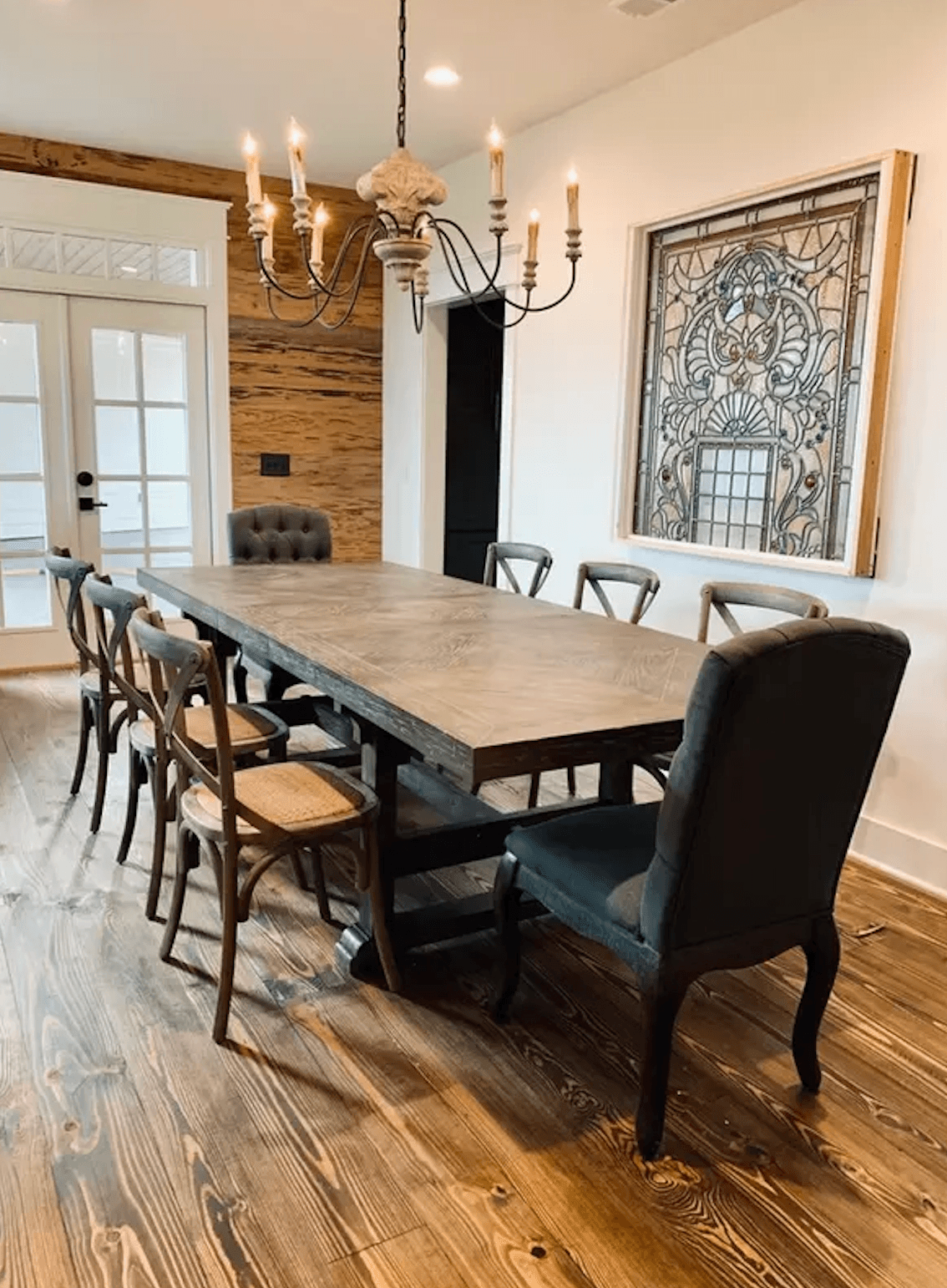 A spacious dining room features a long wooden table with various chairs and a decorative chandelier.