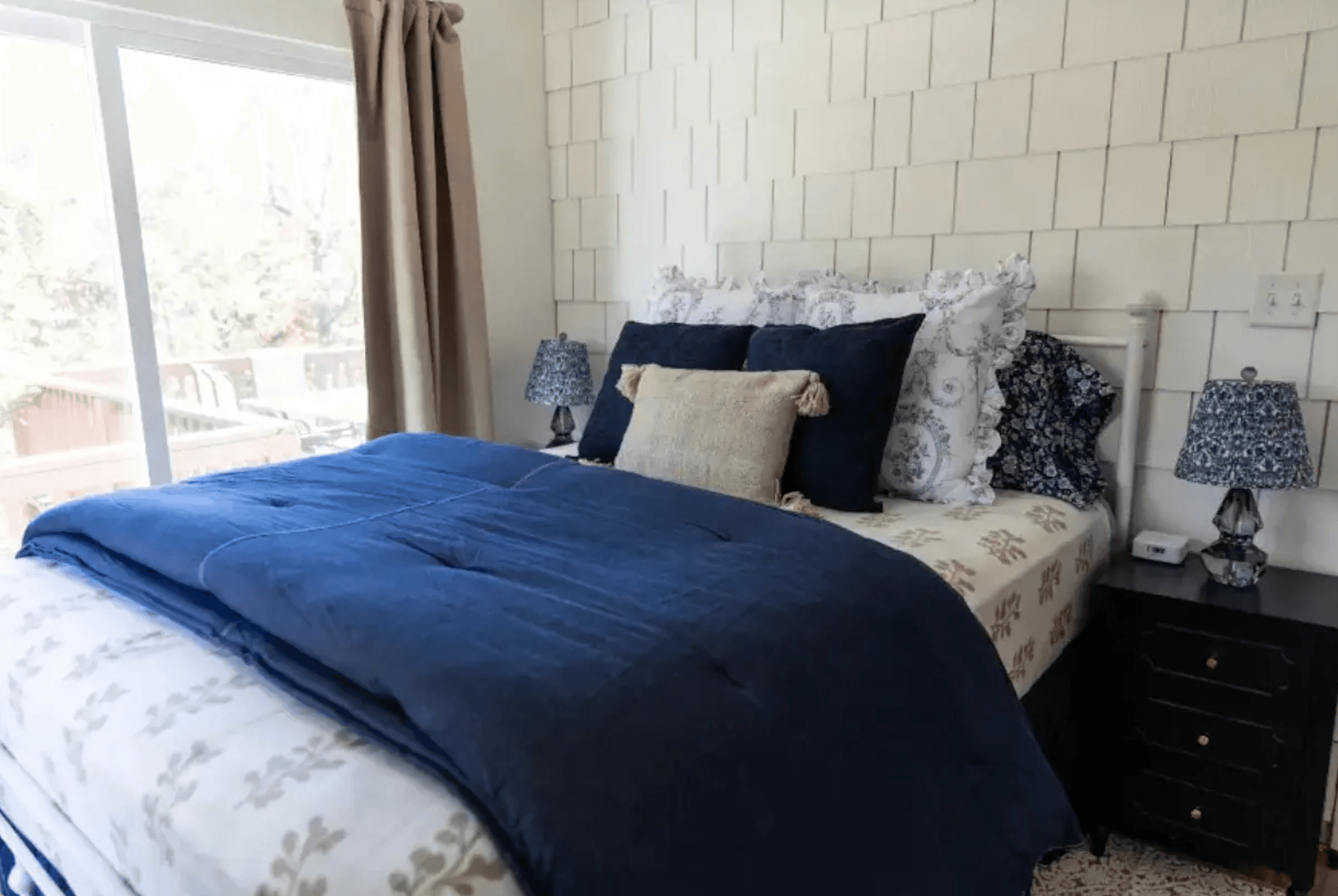 Cozy bedroom featuring a neatly made bed with navy bedding and decorative pillows beside nightstands with lamps.