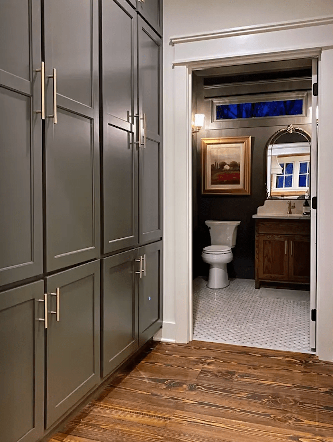 A modern bathroom entrance featuring gray cabinetry, a toilet, and a sink area with a mirror.