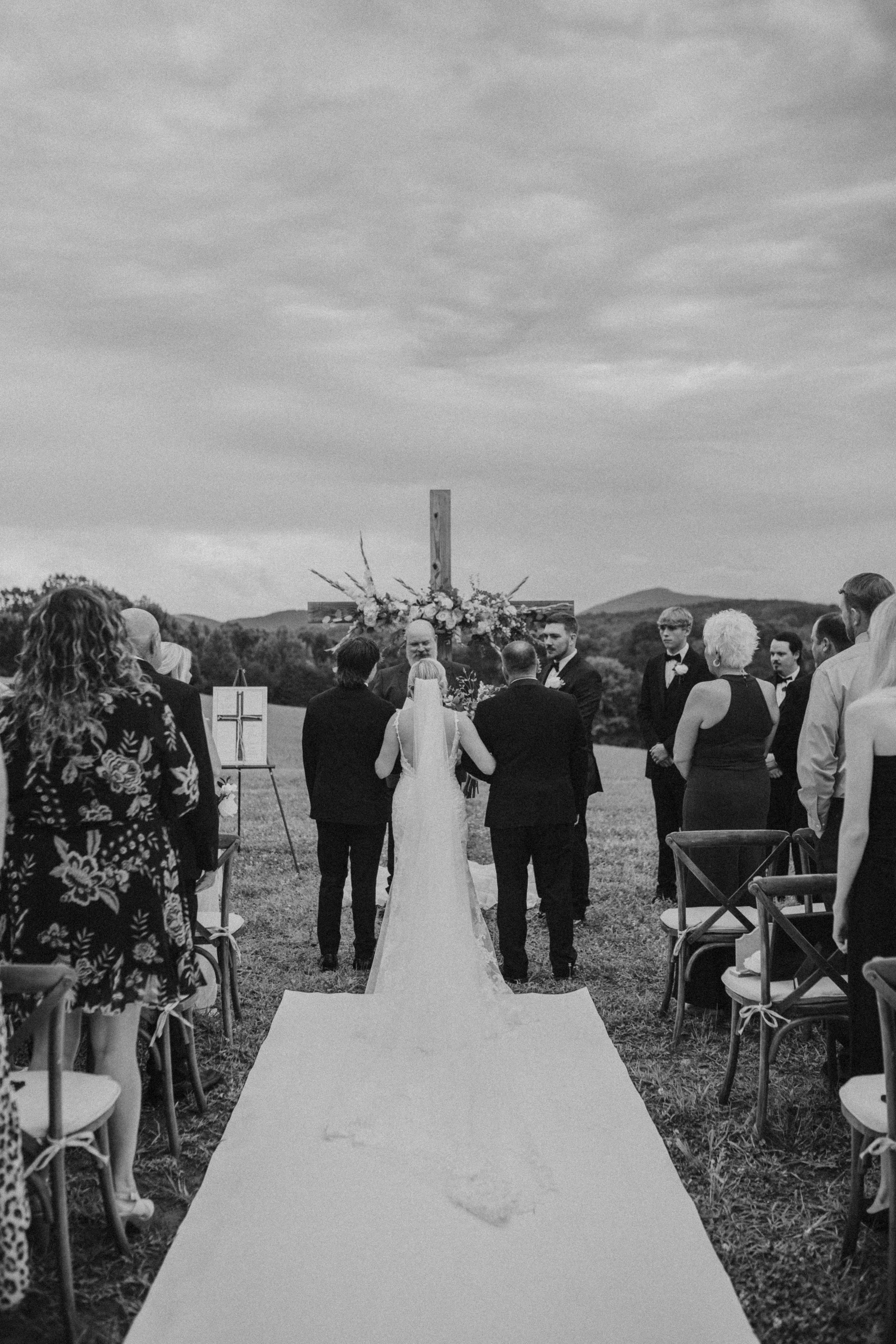 A bride and groom stand before an officiant at an outdoor wedding ceremony with guests seated nearby.
