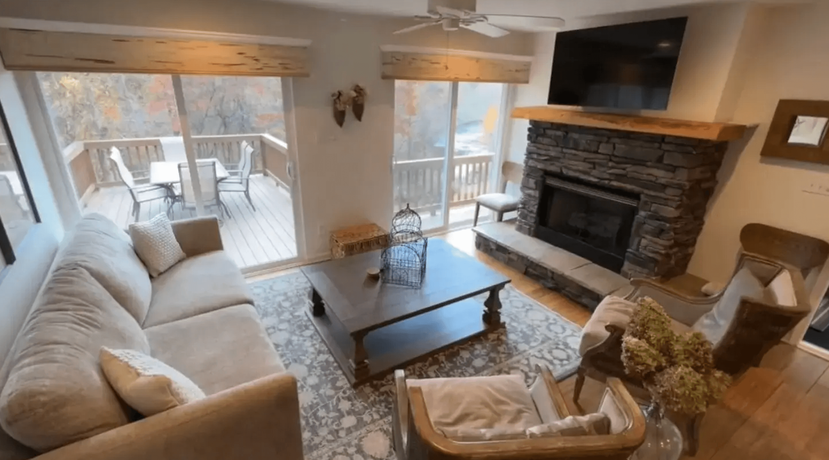 Cozy living room featuring a stone fireplace, modern furniture, and large windows leading to an outdoor deck.