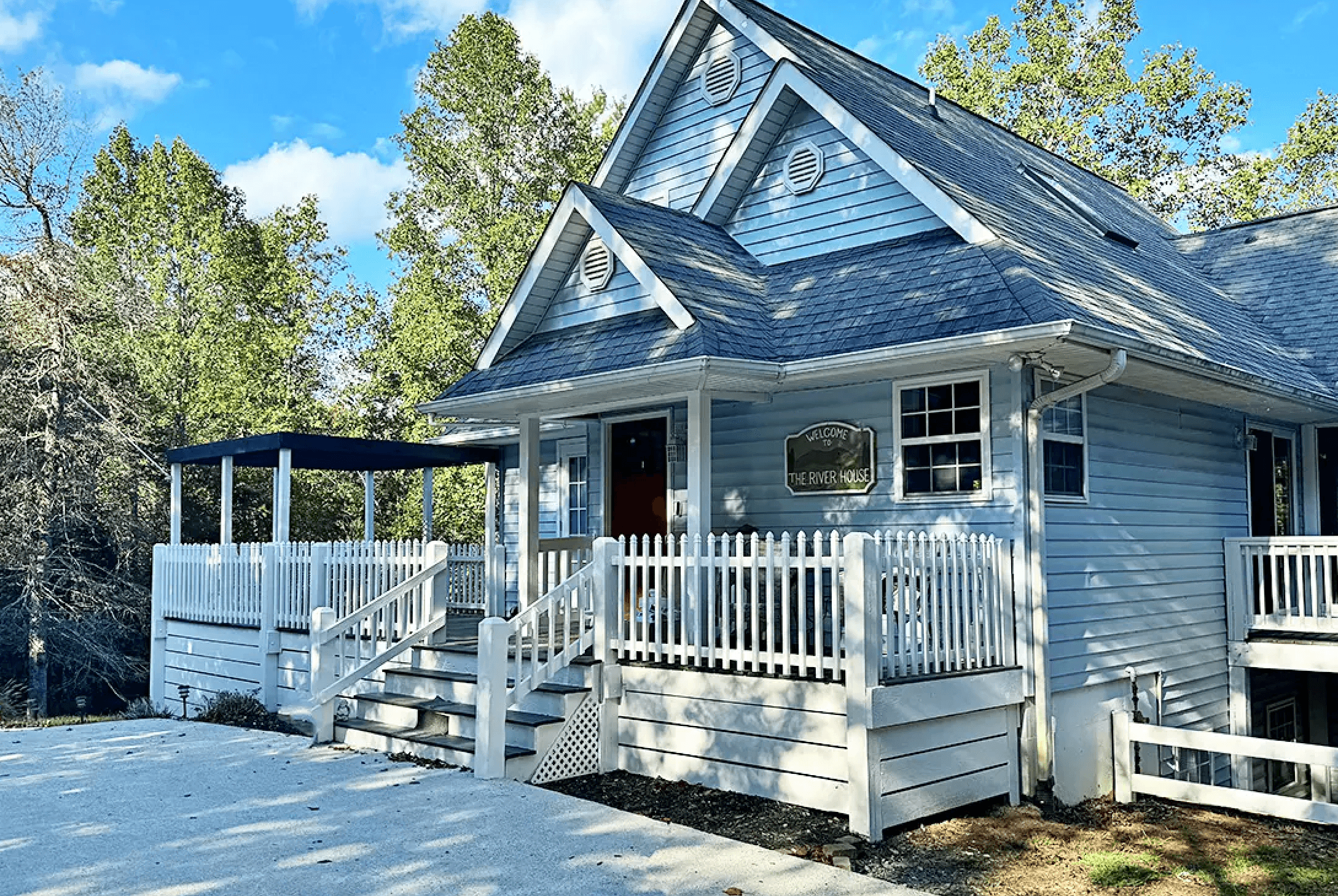 A light blue house with white railings surrounded by trees.