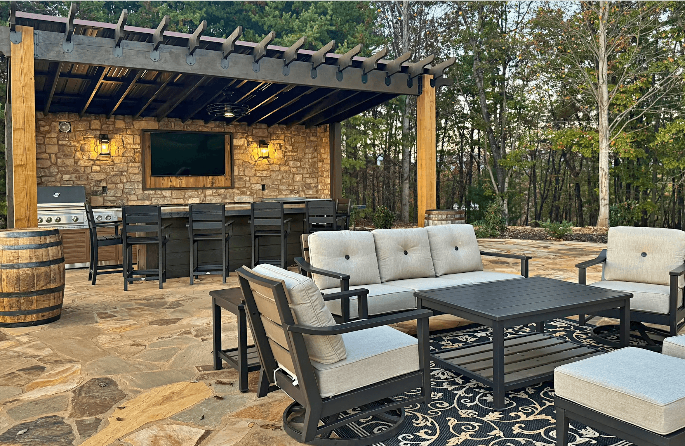 Outdoor seating area with a stone grill, bar, and shaded pergola.