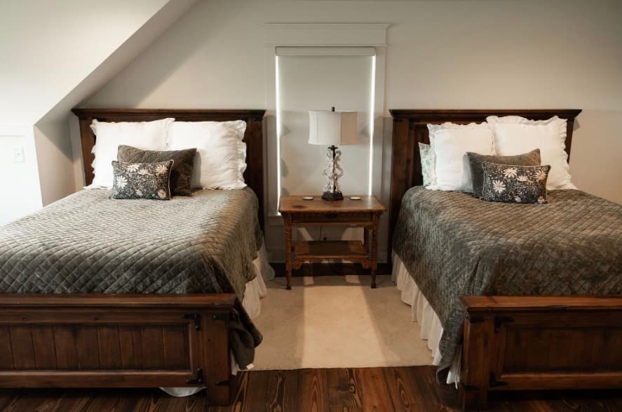 A cozy bedroom featuring two wooden twin beds with gray blankets, flanked by a wooden nightstand and a lamp.