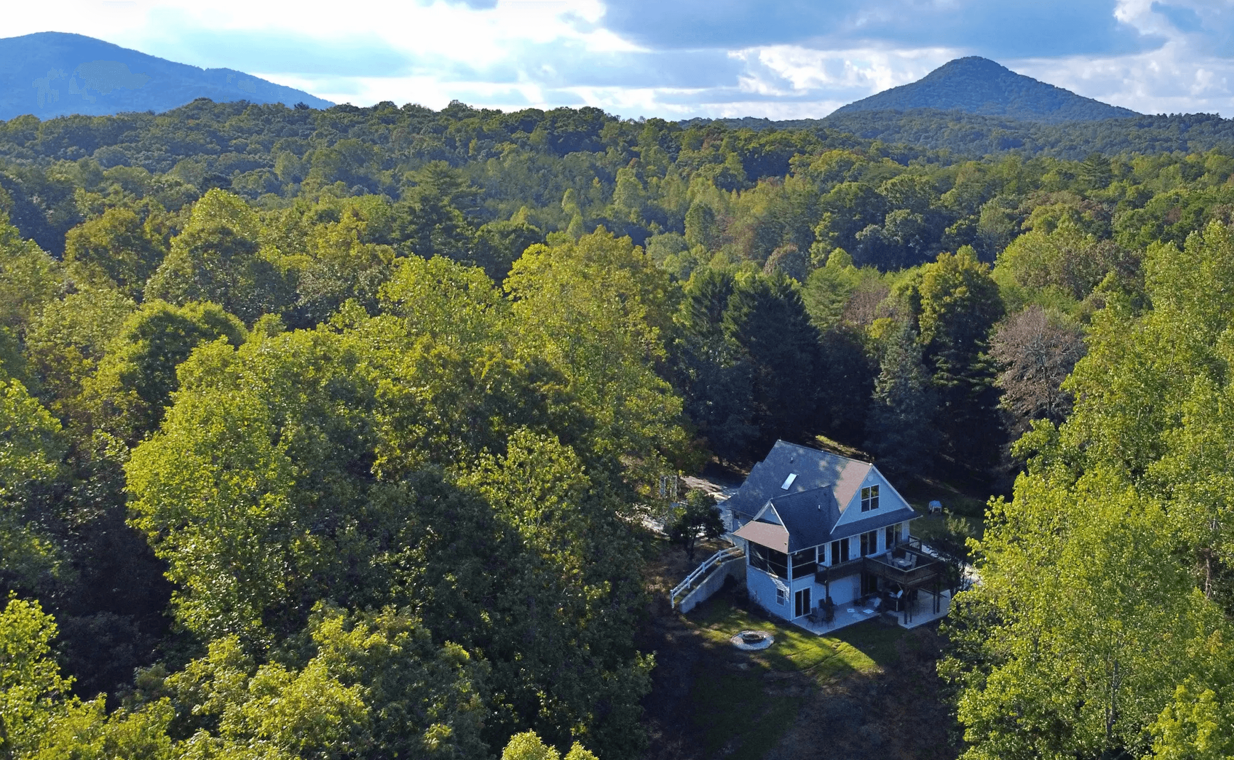 Aerial view of a house surrounded by lush green trees and mountains in the background.