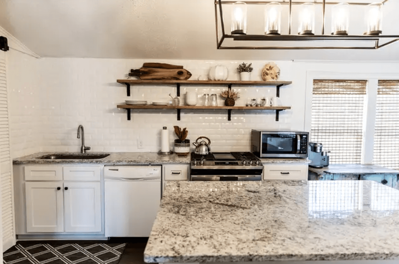 Modern kitchen featuring granite countertops, white cabinetry, open shelving, and stainless steel appliances.
