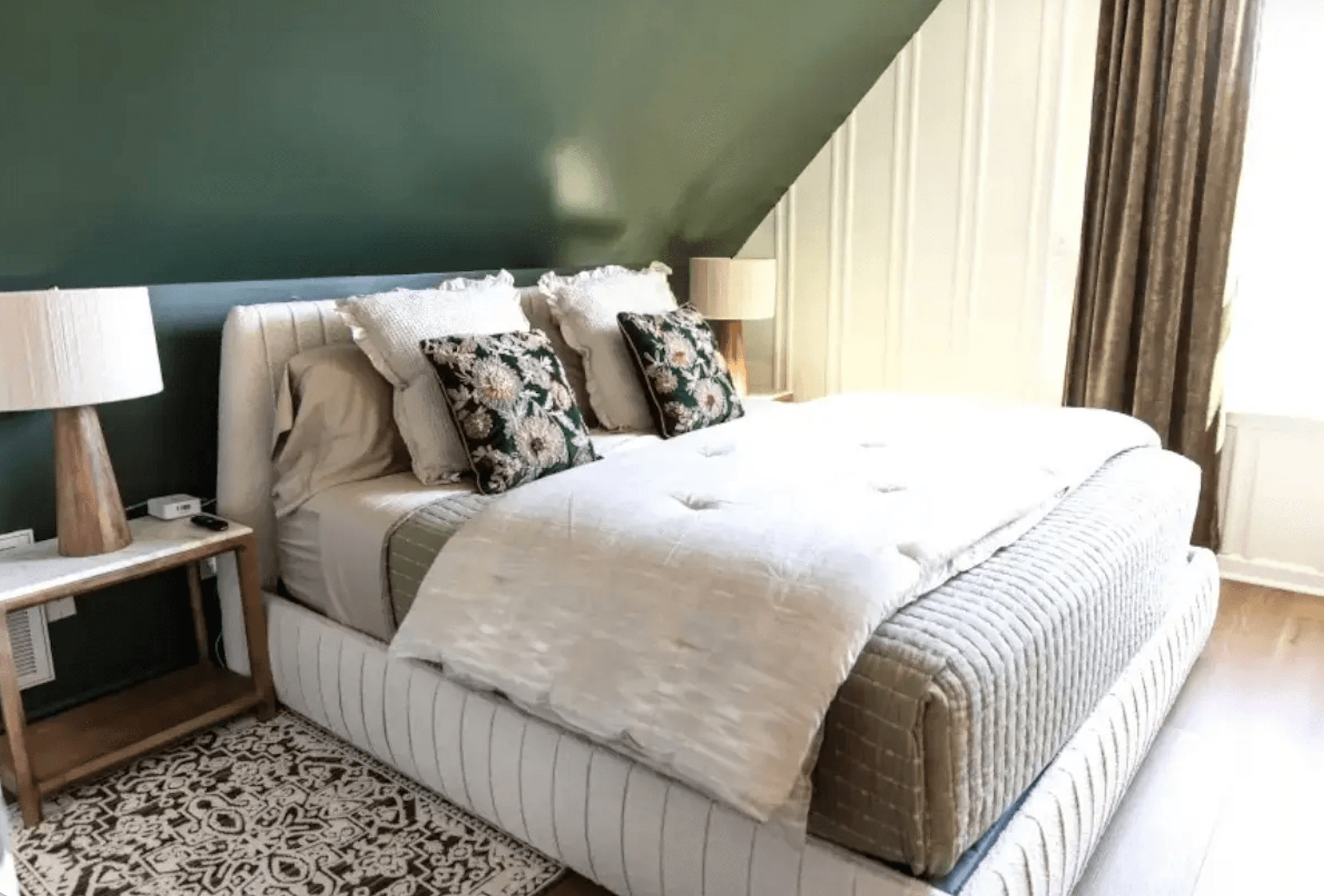 A cozy bedroom with a green accent wall, a plush bed, decorative pillows, and wooden side tables.