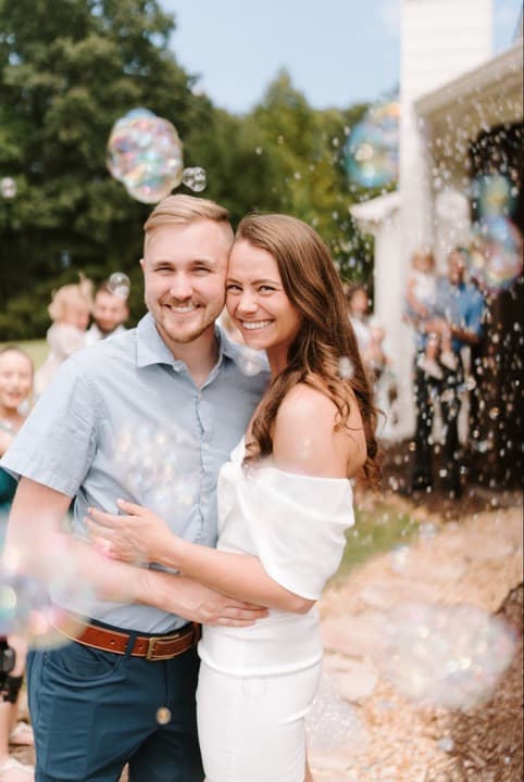 A happy couple embraces amid bubbles and joyful guests at an outdoor celebration.