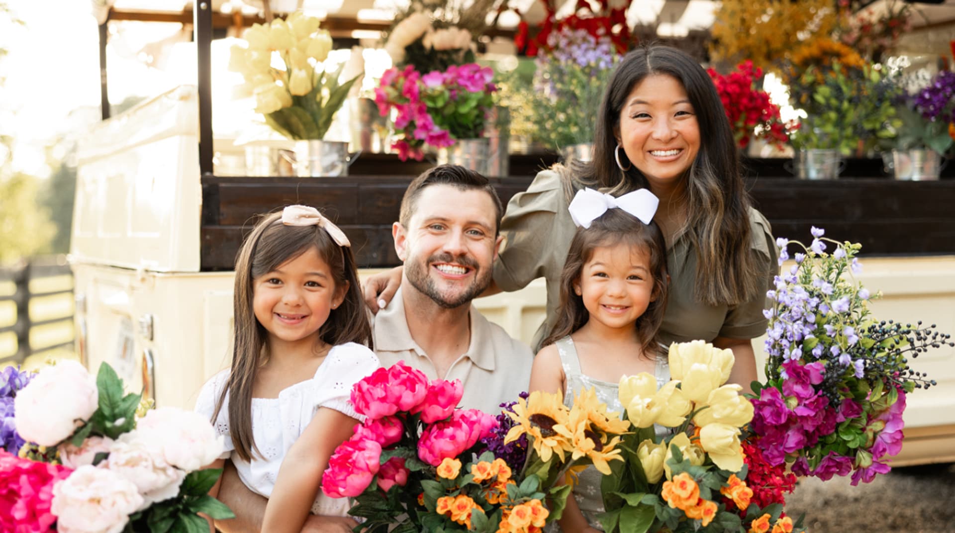 A smiling family of four holds colorful flowers at a flower market.