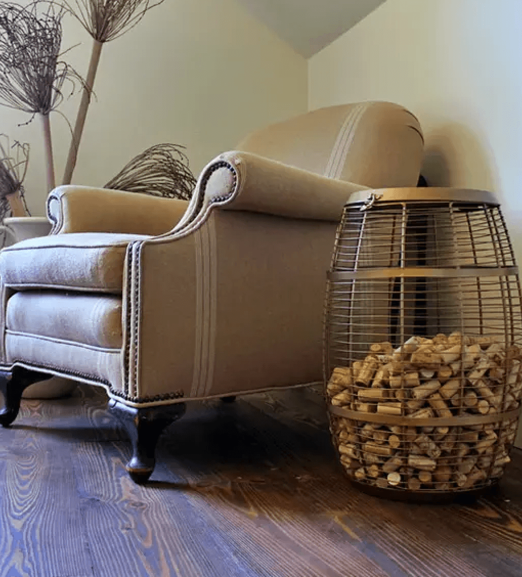 A beige upholstered armchair beside a wire basket filled with wine corks.