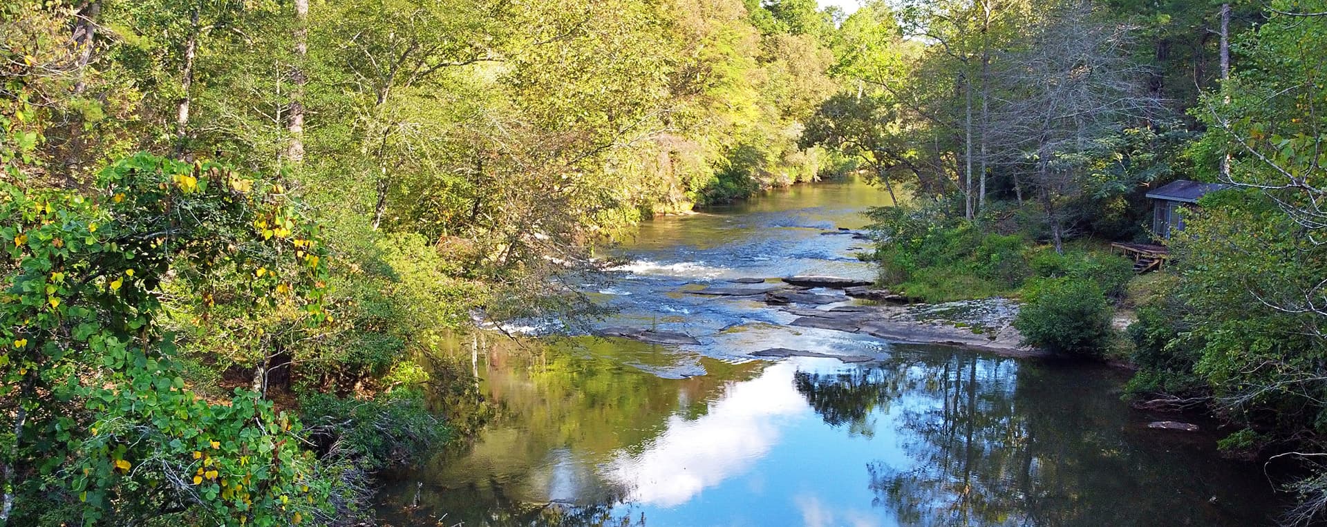 A serene river flows through lush greenery under a clear blue sky.