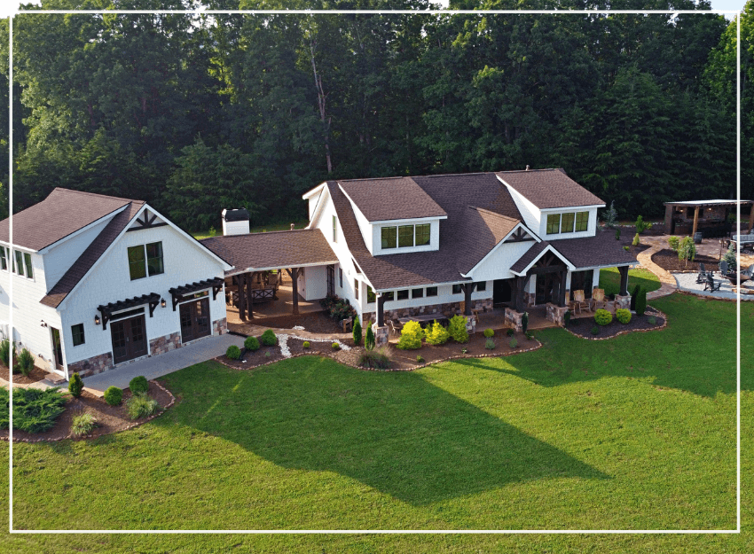Aerial view of a modern two-story house surrounded by lush greenery and landscaped yard.