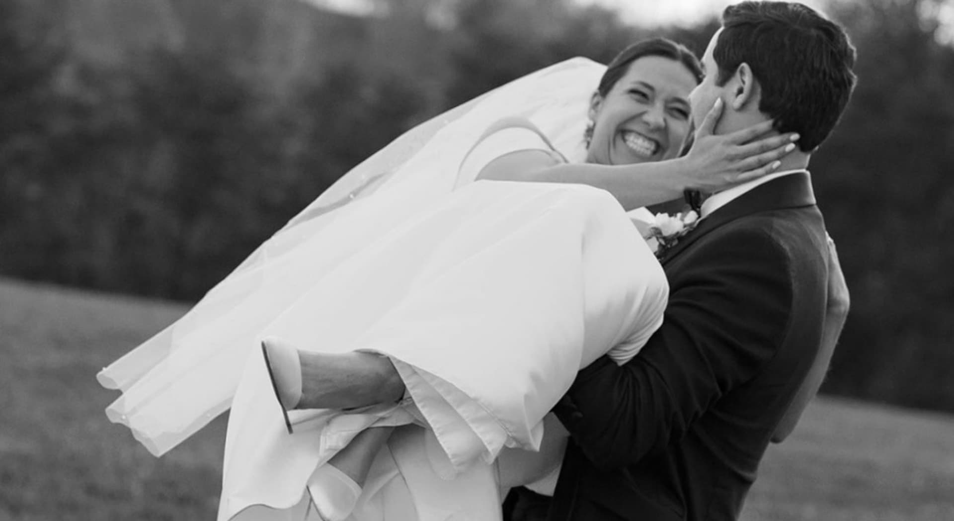 A joyful bride is being lifted by her groom in a picturesque outdoor setting.
