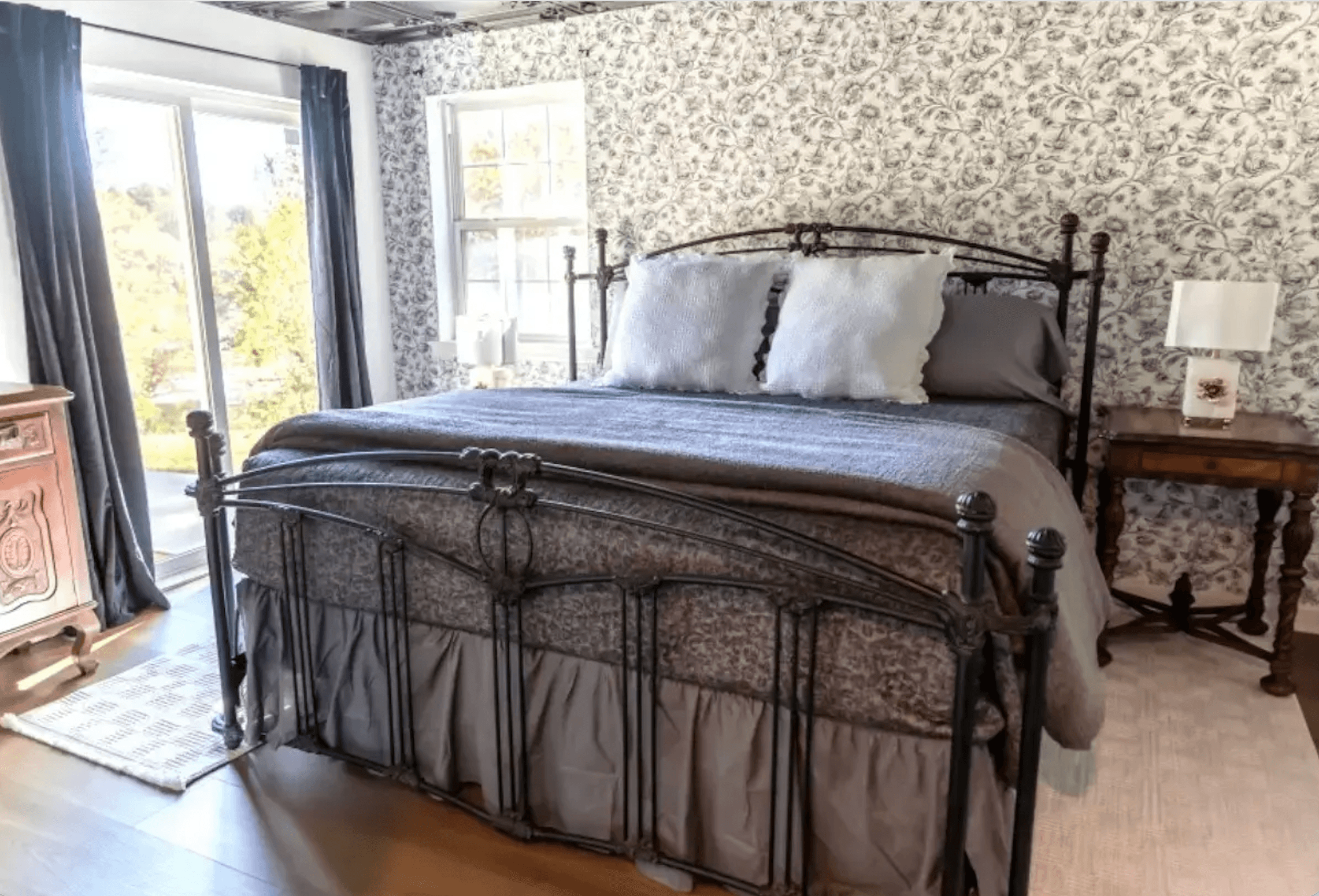 A cozy bedroom featuring a wrought iron bed with gray bedding and floral wallpaper.