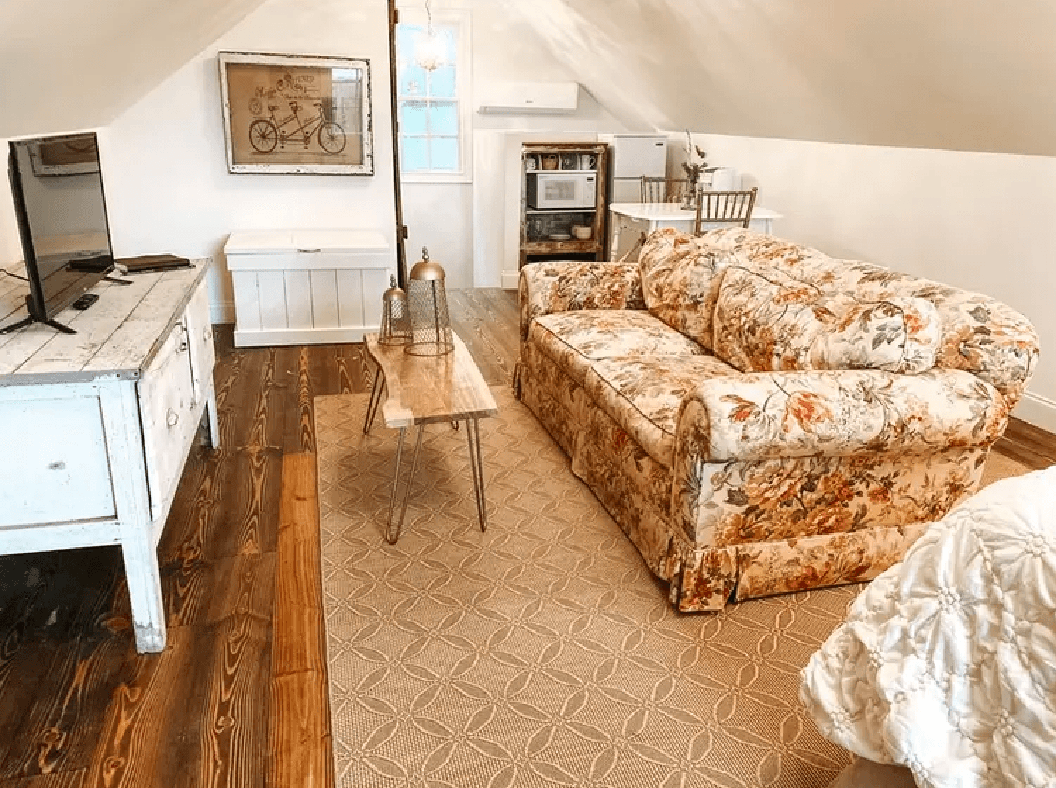 Cozy attic living space with a floral sofa, wooden floor, and simple furnishings.