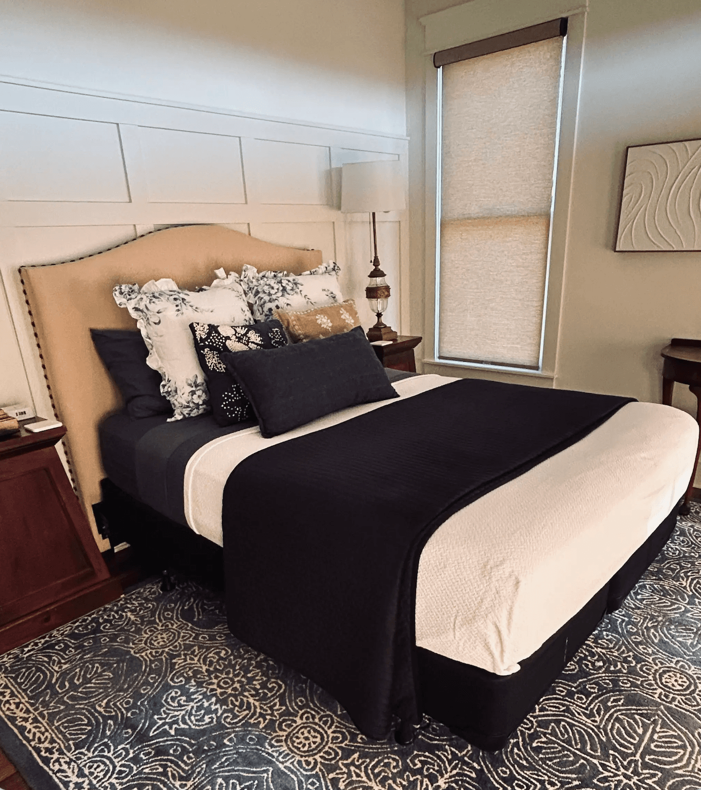 A cozy bedroom featuring a neatly made bed with decorative pillows and a lamp beside a window.