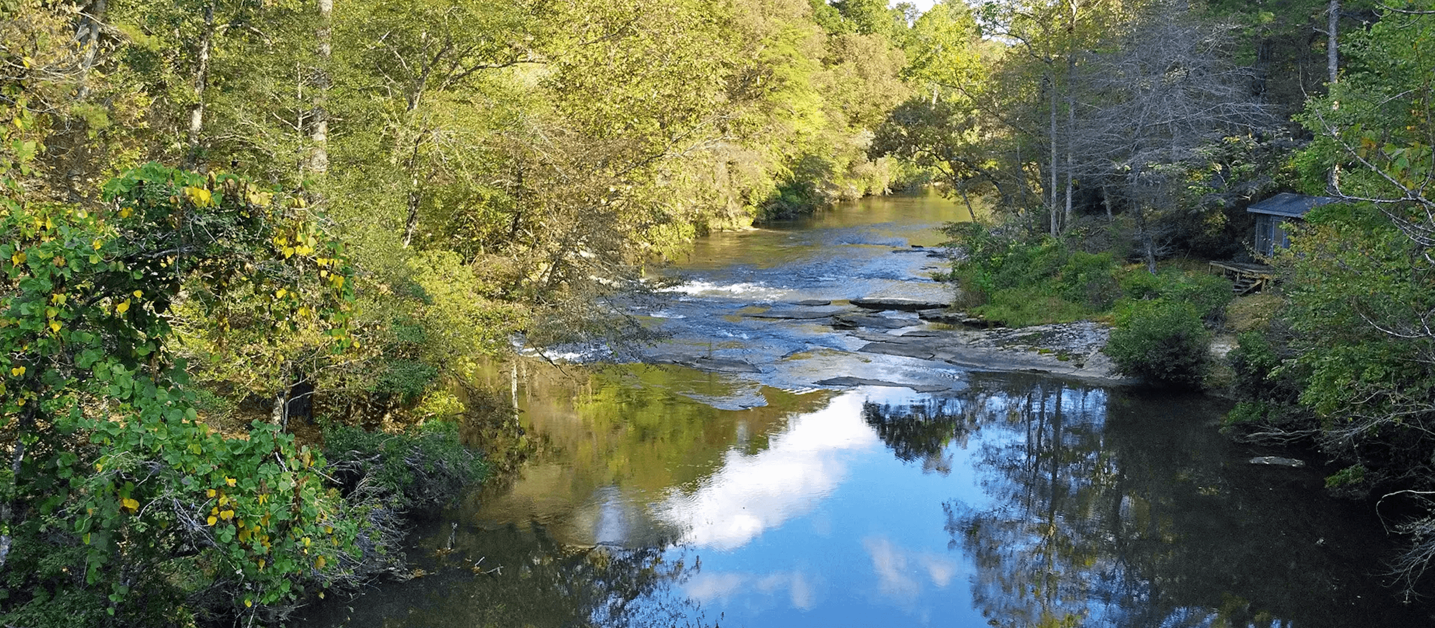 A serene river flows through lush greenery, reflecting the trees and sky above.