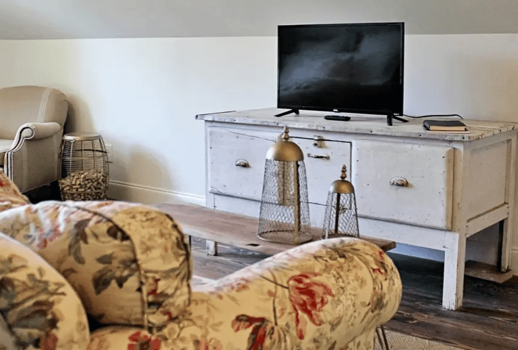 Cozy living space featuring a floral couch, a vintage TV stand, and decorative items.