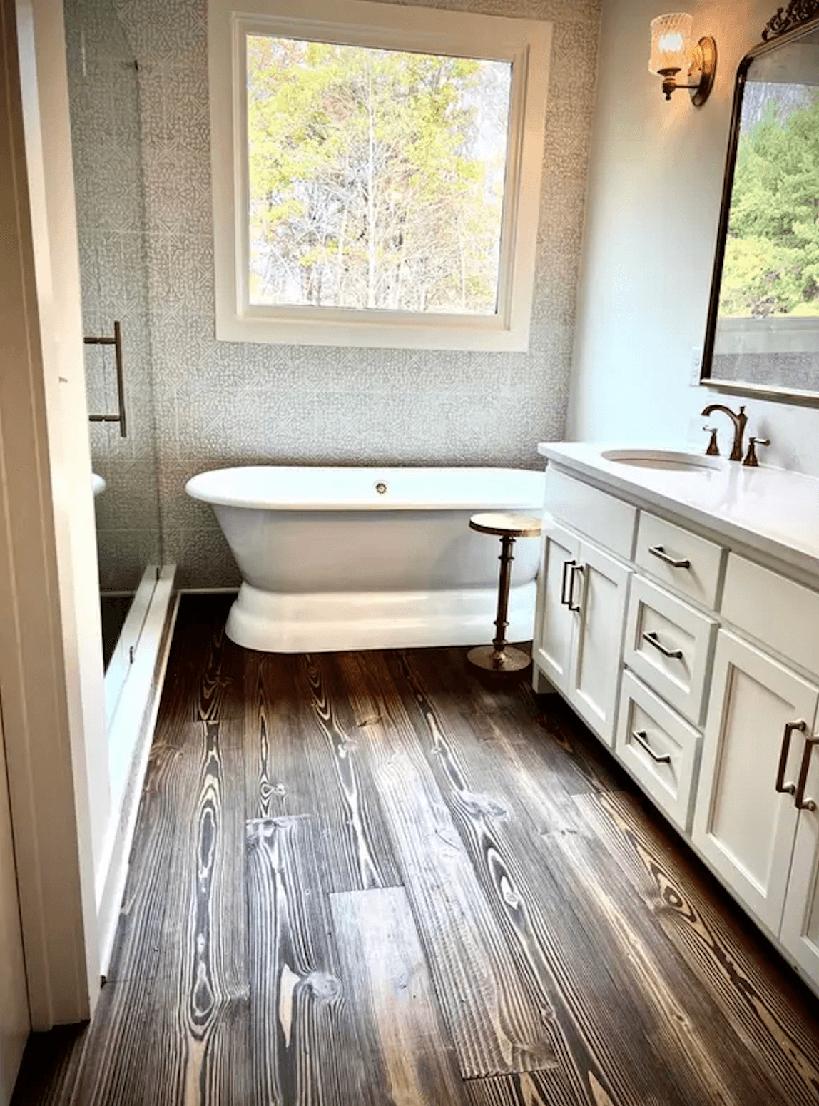 A modern bathroom featuring a freestanding tub, wooden flooring, and a large window.