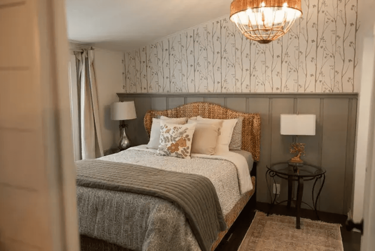 Cozy bedroom with a woven headboard, patterned wallpaper, and soft lighting.