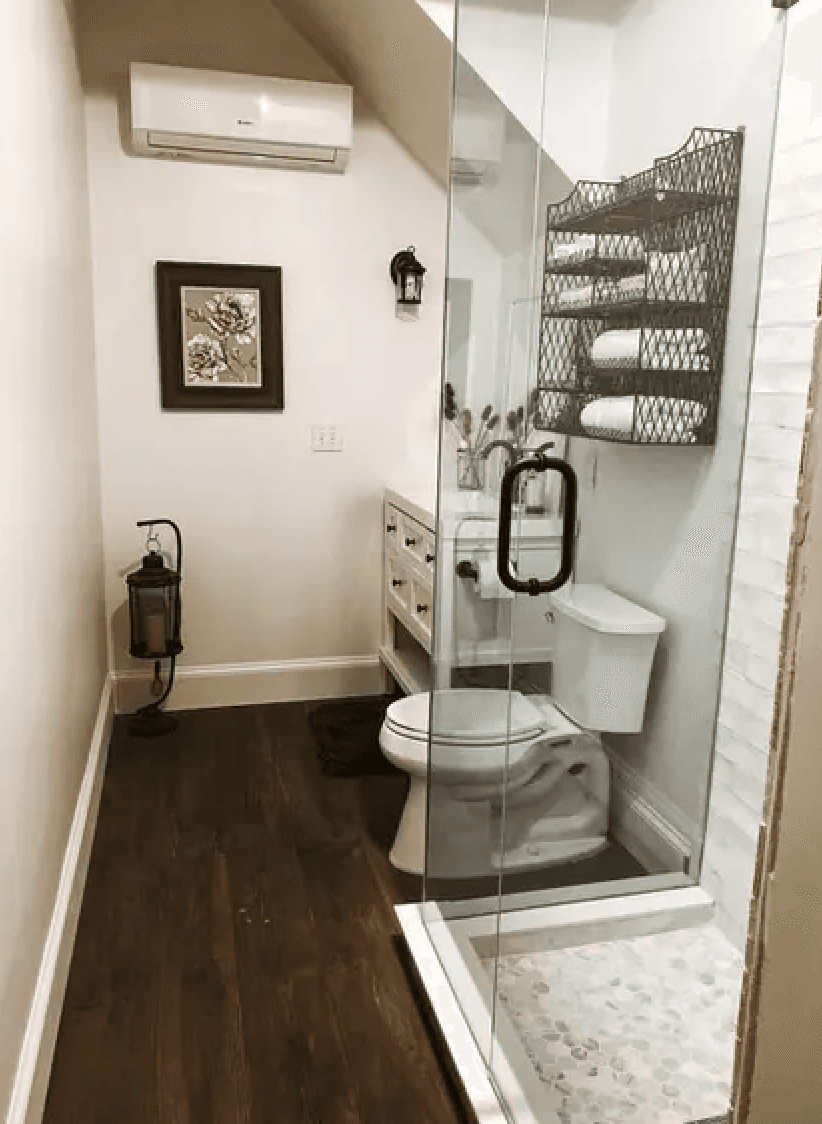 A modern bathroom featuring a glass shower, toilet, wooden flooring, and decorative towel storage.