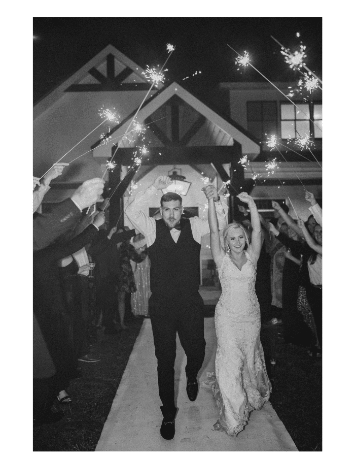 A bride and groom joyfully exit their wedding celebration, surrounded by guests holding sparklers.
